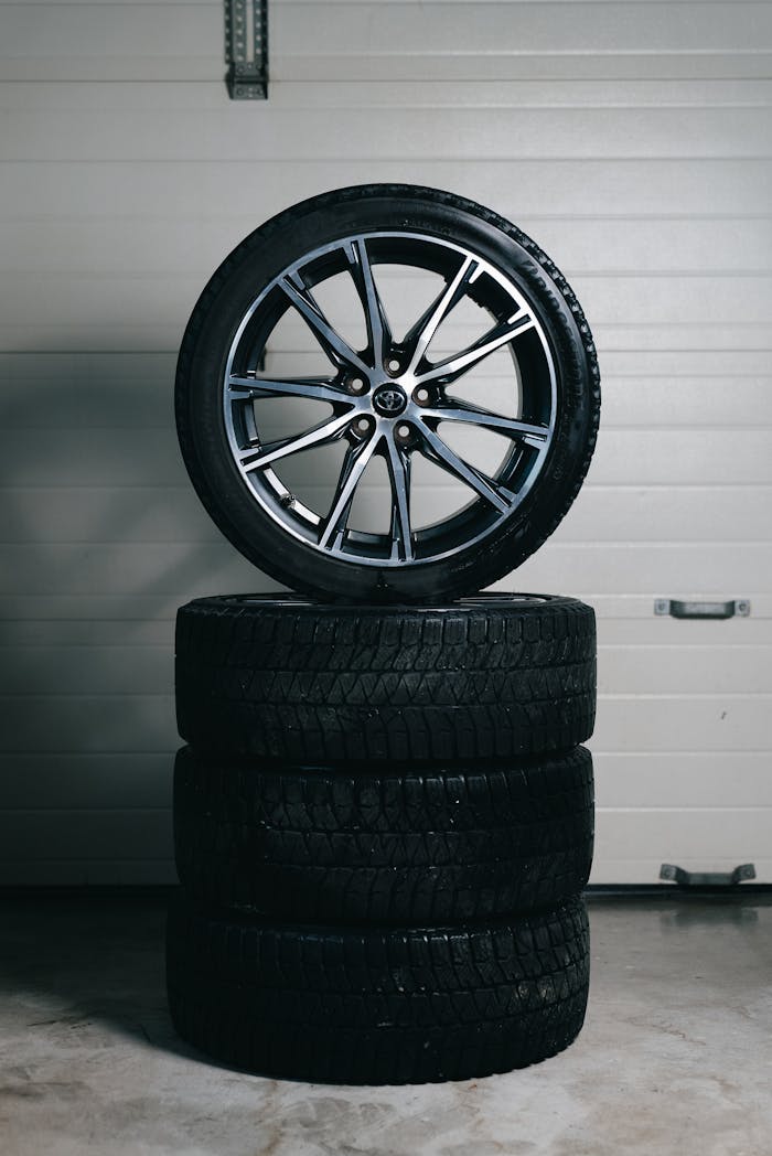 why-choose-us Car tires stacked with an alloy wheel on top in a garage setting. Perfect for automotive themes.