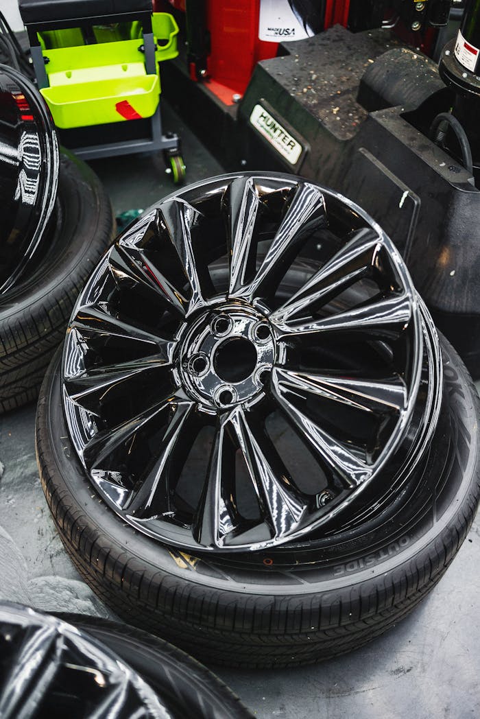 gallery-3 Glossy black car wheel rim and tire stack in an automotive workshop.